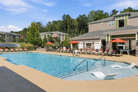 A large swimming pool with lounge chairs and umbrellas in front of a resort-style building.