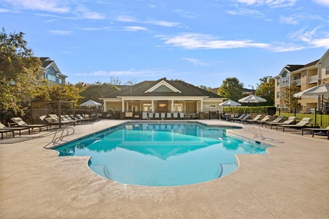 A large outdoor swimming pool surrounded by lounge chairs and a building in the background.