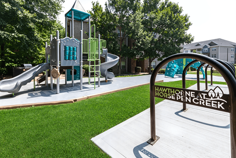 A playground in Hawthorne at Pinecreek with a green slide and a grey slide.