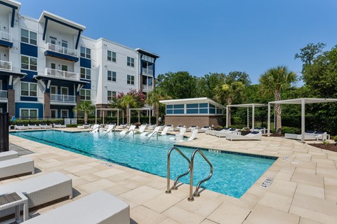 A swimming pool surrounded by lounge chairs and apartment buildings.