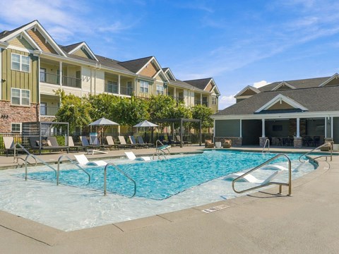 A swimming pool surrounded by lounge chairs and umbrellas in front of apartment buildings.