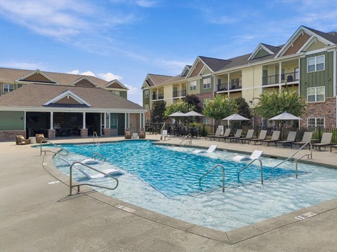 A large swimming pool with lounge chairs and umbrellas in front of apartment buildings.