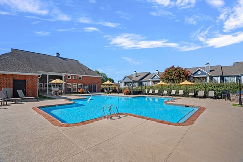 A swimming pool surrounded by a concrete patio and lounge chairs.