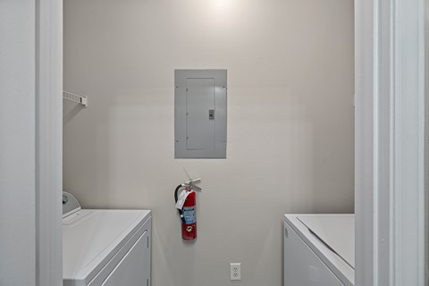 A white laundry room with a red fire extinguisher hanging on the wall.