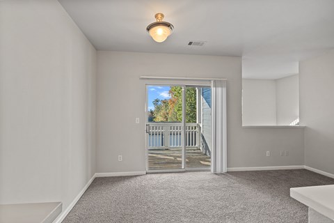 A room with a carpet floor and a window overlooking a deck.