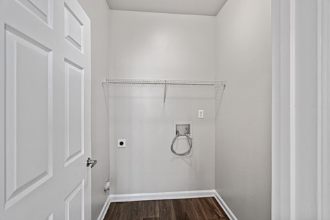 A white door is on the left and a white wall with a towel ring and a shelf is on the right.