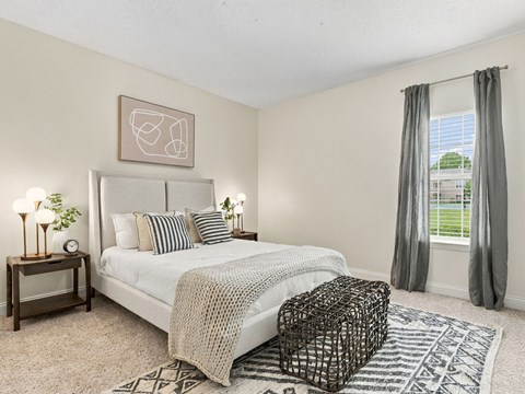 A bedroom with a large bed, a nightstand with a lamp, and a window with curtains.