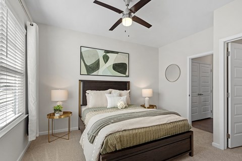 A bedroom with a bed, a ceiling fan, and a painting on the wall.