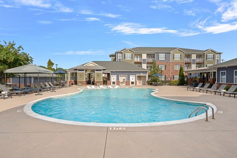 A large swimming pool in front of a building with lounge chairs around it.