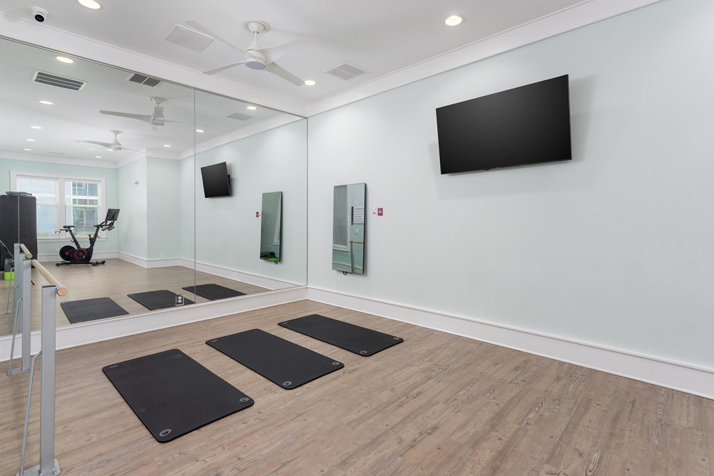 A room with a mirror, a television, and yoga mats on the floor.