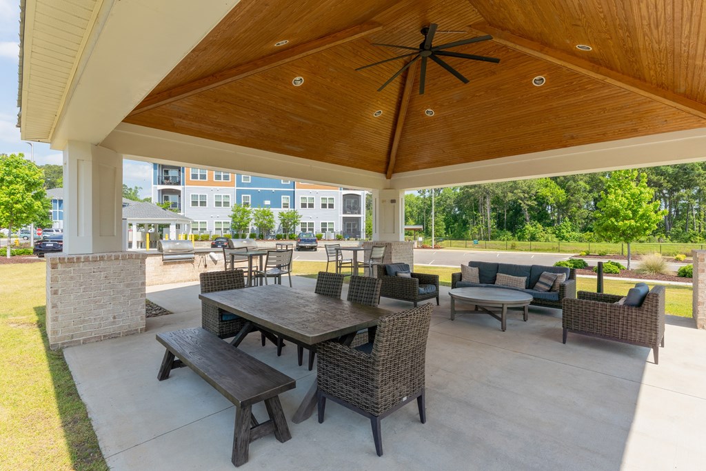 A patio with a table and chairs under a wooden roof.
