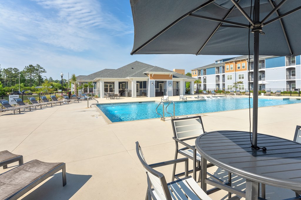 A pool area with a table and chairs and a building in the background.
