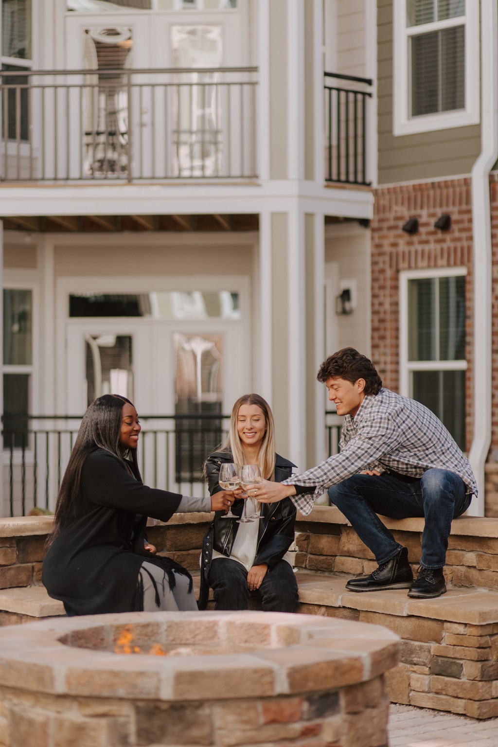 Three people sitting around a fire pit outside a house.