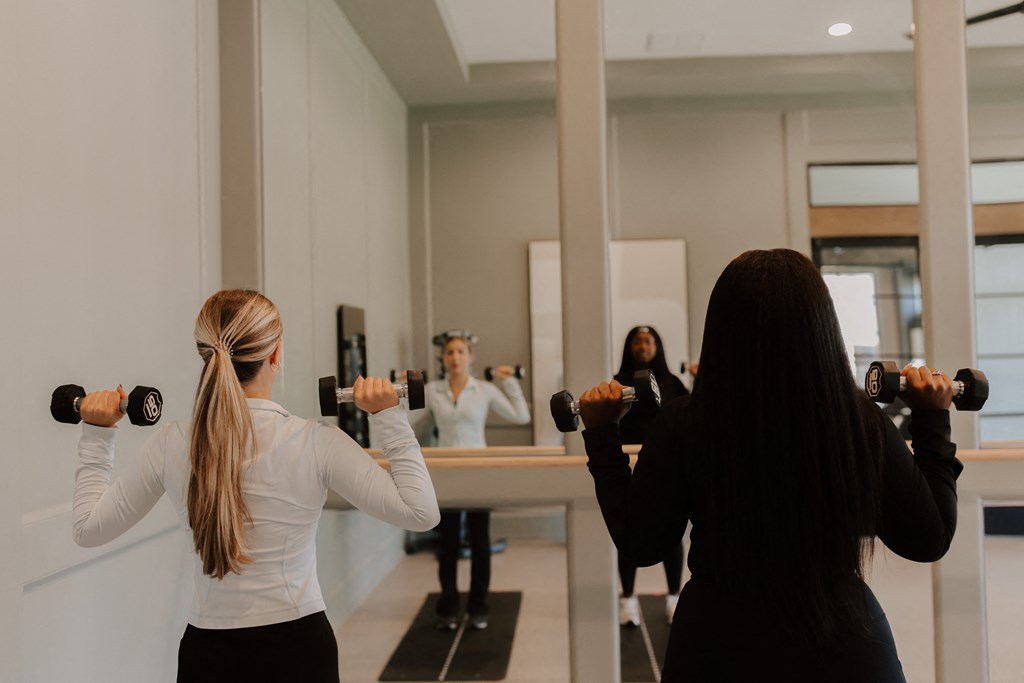 Three women are working out with dumbbells in a gym.