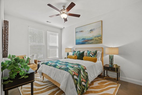 A bedroom with a bed, a ceiling fan, and a painting on the wall.