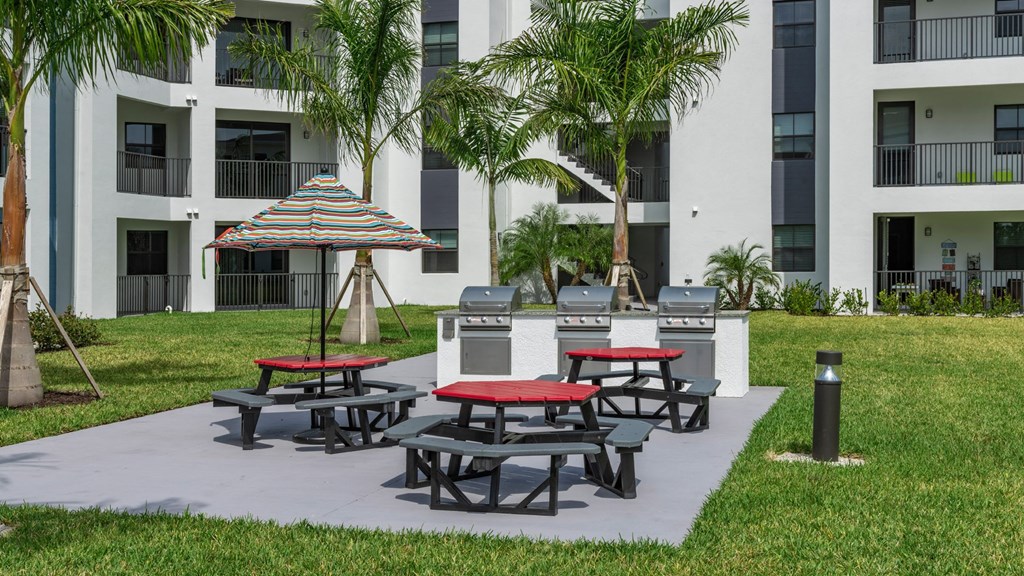 a patio with picnic tables and barbecue grill in front of an apartment building