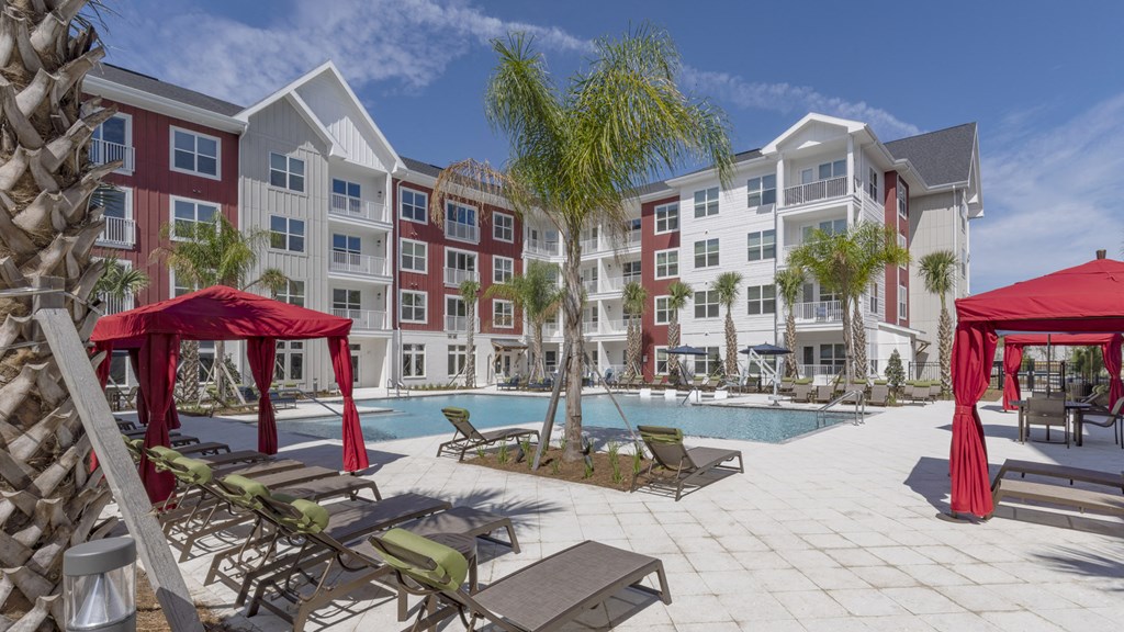 an outdoor pool area with chairs and umbrellas in front of an apartment building