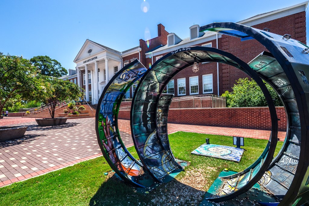 A large, circular, outdoor sculpture is in the foreground of a brick building.