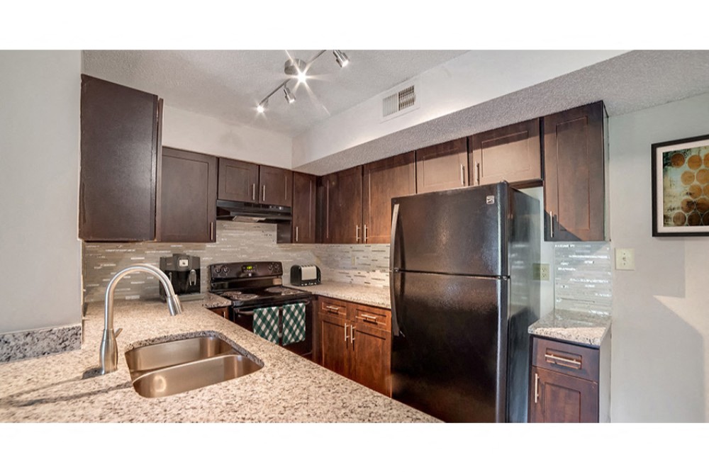 Dark wood kitchen cabinetry with a black refrigerator and tile backsplash at Midora at Woodmont in Tamarac, FL