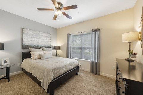 A bedroom with a bed, a ceiling fan, and a window with curtains.