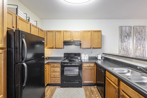 A black refrigerator stands in a kitchen with wooden cabinets and a black stove.