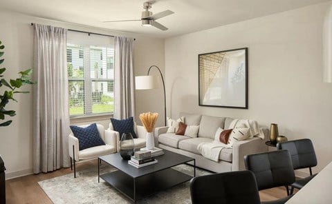 A living room with a grey couch, a black coffee table, and a large window with curtains.