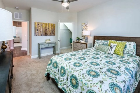 A bedroom with a patterned bedspread and a ceiling fan.