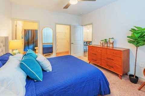 A bedroom with a blue bedspread and a wooden dresser.