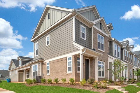 A large, modern house with a grey and brown exterior and a well-maintained lawn.