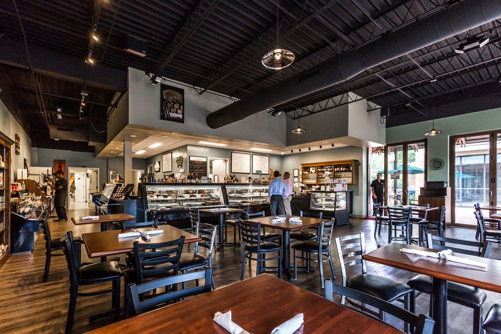 A restaurant with wooden tables and chairs and people standing in the background.