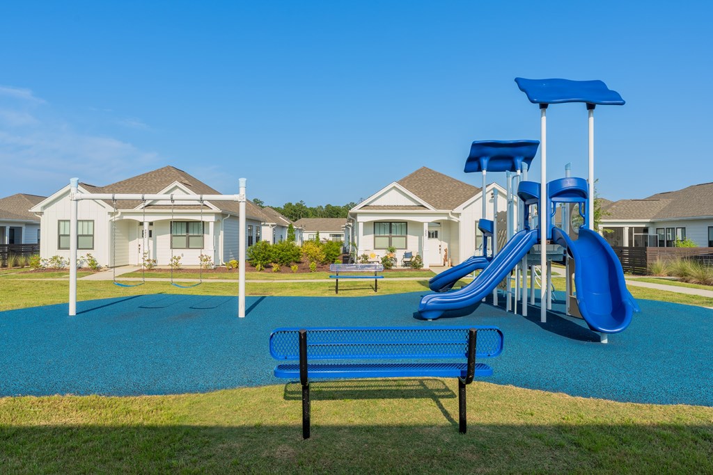 A playground with a blue slide and a bench in front of a row of houses.