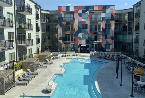 A large swimming pool surrounded by lounge chairs and buildings with a colorful mural.