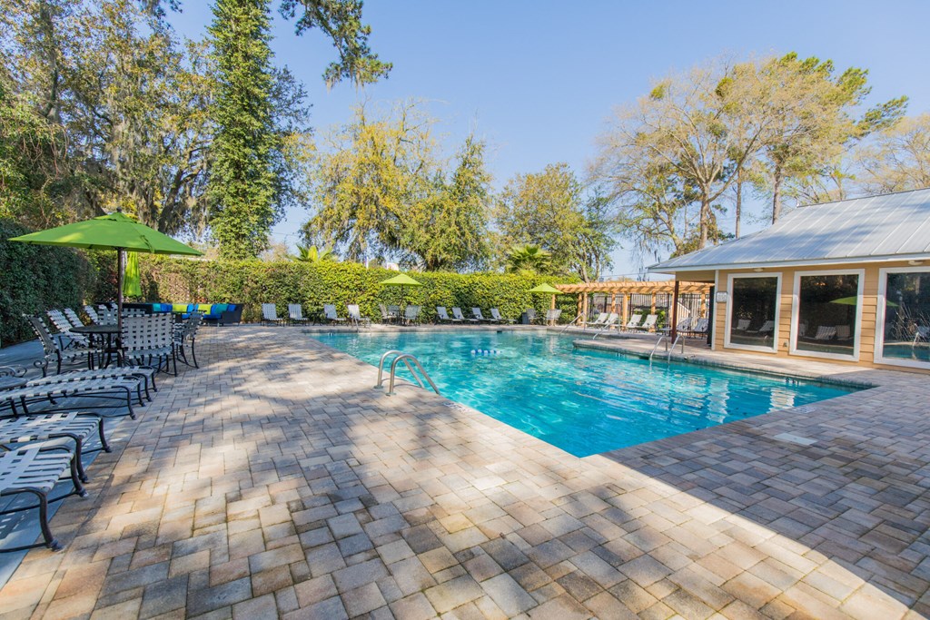 a swimming pool with chairs and umbrellas next to a house