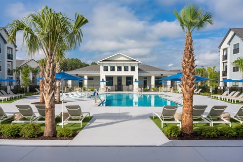 A pool surrounded by palm trees and lounge chairs at Evolve Holly Ridge Partments in Holly Ridge, NC