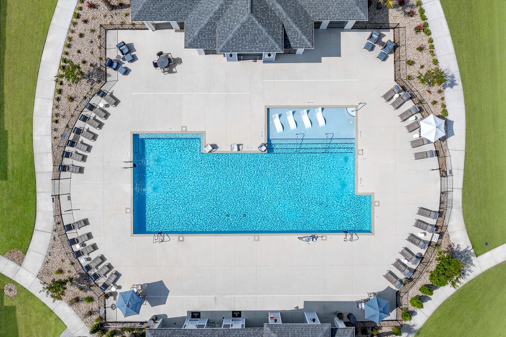 A large swimming pool surrounded by a grassy area and a building.