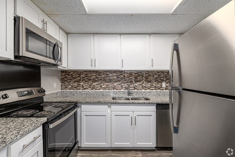 A kitchen with a stainless steel refrigerator and a stone backsplash.
