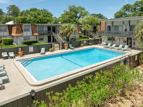A pool surrounded by chairs and trees.