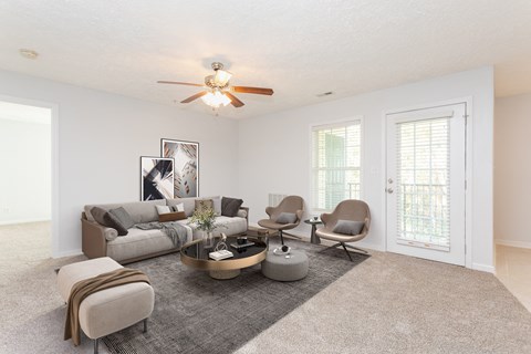A living room with a grey sofa, a grey armchair, a grey ottoman, a coffee table, and a ceiling fan.
