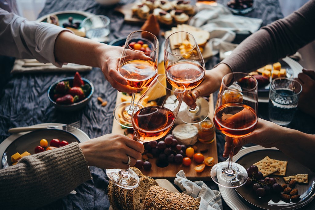 A group of people toasting with glasses of wine at a table filled with various foods.
