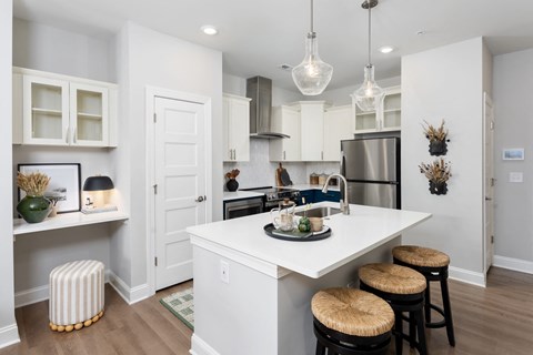A kitchen with white cabinets and a white island with two stools.