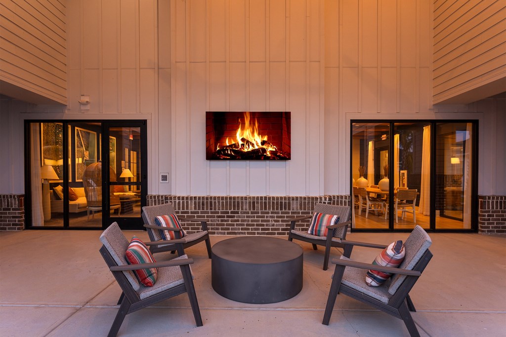 A fireplace is on the wall above a fire pit in a patio.