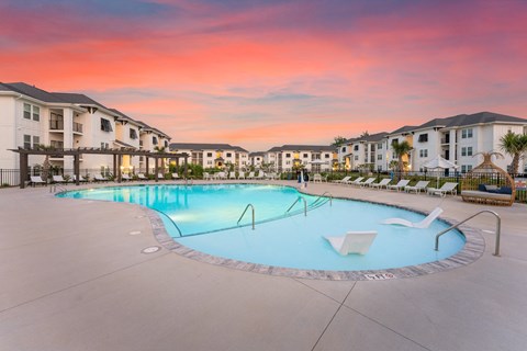 A swimming pool surrounded by lounge chairs and buildings in the background at Monument at Ocean and Main in Shallotte, NC..