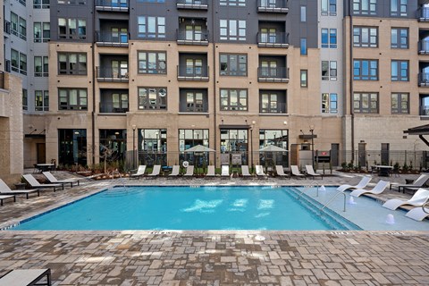 A swimming pool surrounded by lounge chairs in front of a building.