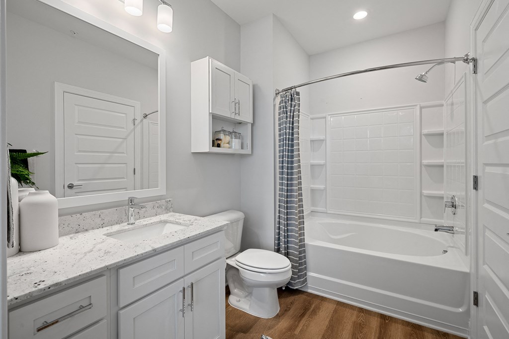 a bathroom with white cabinets and a white toilet next to a white bathtub with a shower