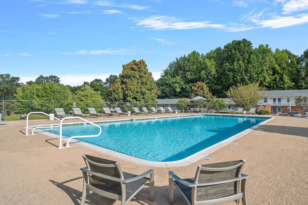 a swimming pool with chairs around it and trees in the background