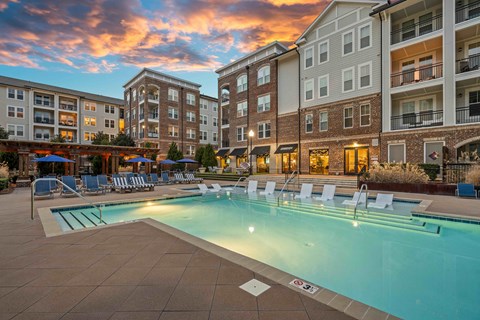 A swimming pool surrounded by lounge chairs and buildings in the background.