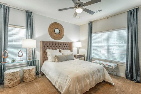 A bedroom with a large bed, a ceiling fan, and a window with curtains.