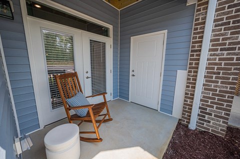 A wooden rocking chair is placed in a sunny room with a white toilet and a white door.