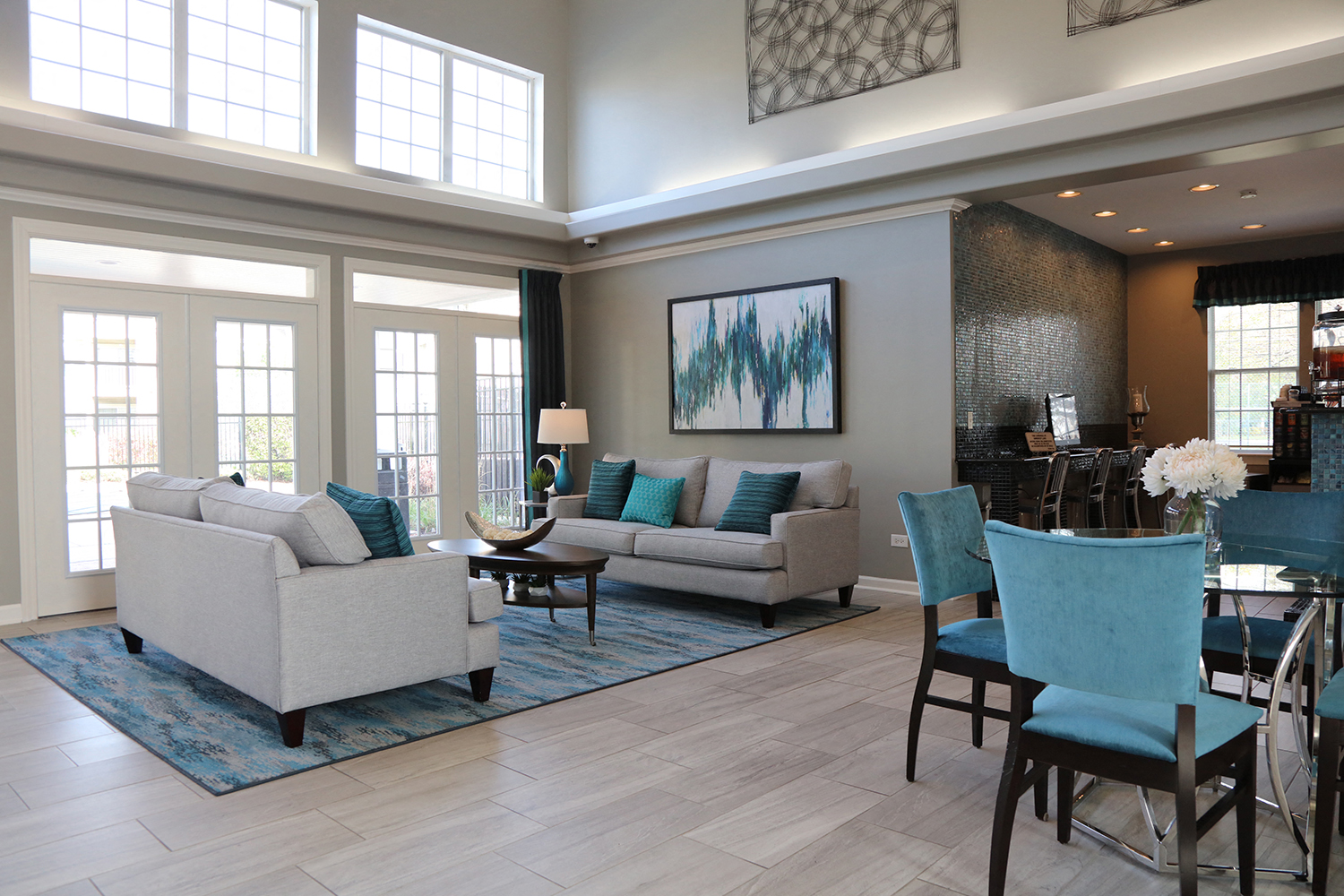 A living room with a white couch, blue chairs, and a painting on the wall.