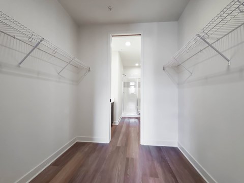A hallway with white walls and wood flooring leading to a door.